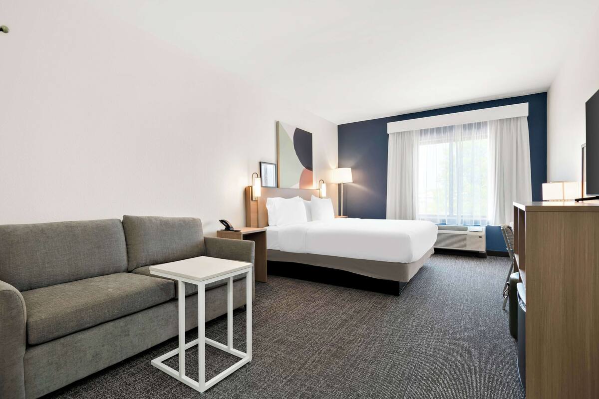 A hotel room with a bed, a sofa, a small table, a desk, and a lamp.