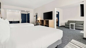 Quarto de hotel com uma cama grande, televisão, sofá e secretária com candeeiro.