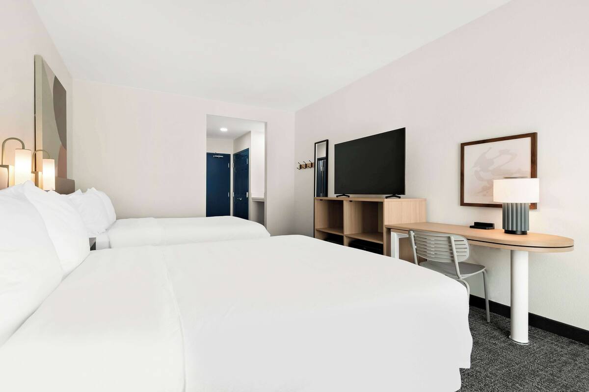 A hotel room with two beds, a desk with a chair, a television, and a lamp.