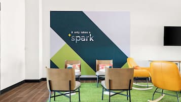 Una habitación con dos sillas marrones, una mecedora amarilla y una alfombra verde. Se ve una pared grande con el texto 'It only takes a spark'.