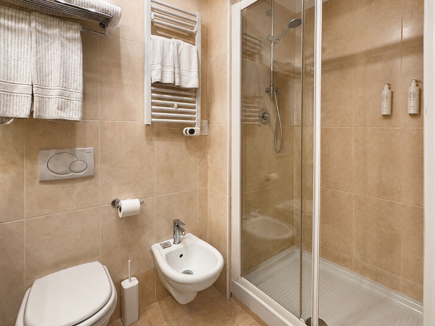 Un baño con inodoro, bidé, toallero y zona de ducha con mampara de vidrio.