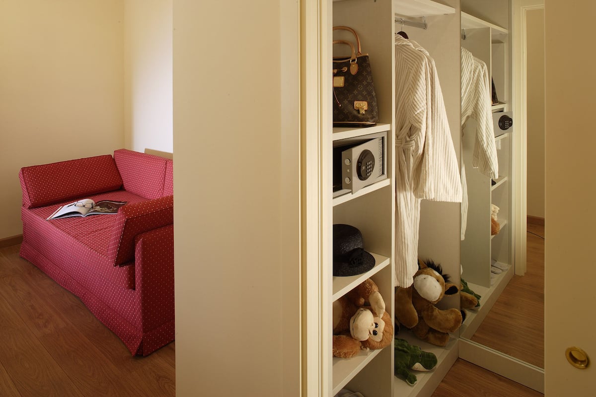 A room with a red sofa, a mirror, and a wardrobe containing clothes and a stuffed toy.