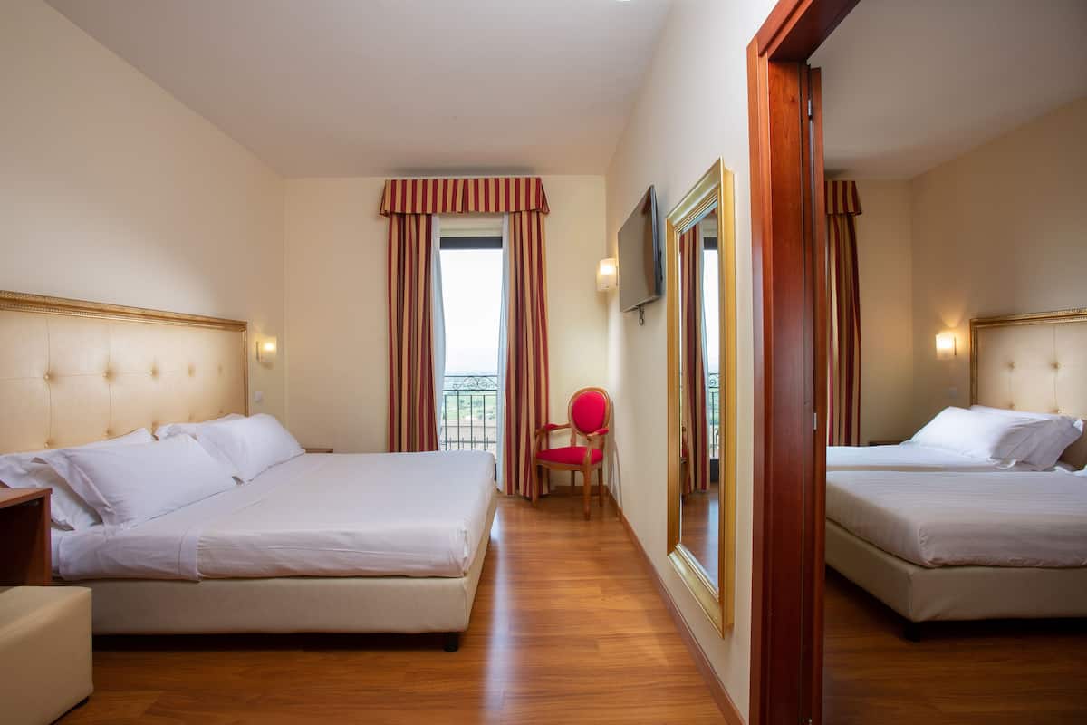 A hotel room with two beds, a chair, a TV, and a balcony view.