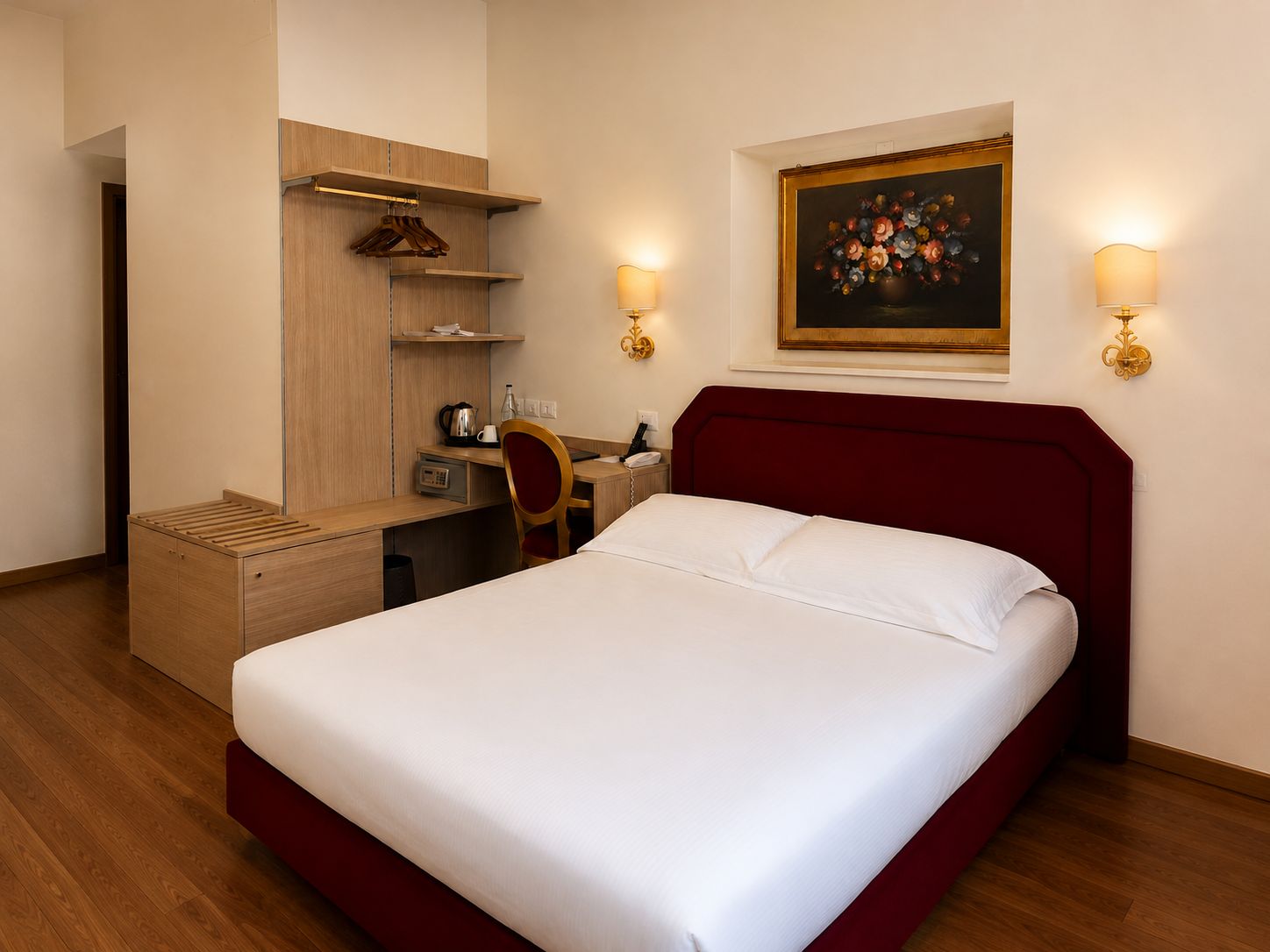 A hotel room with a bed, desk, chair, and a painting on the wall.