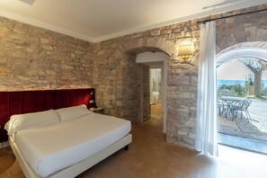 Un dormitorio con pared de piedra, cabecera roja, cama blanca y vistas a un patio exterior.