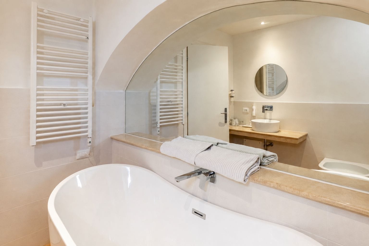 A modern bathroom with a freestanding bathtub, a large mirror, and a vanity with a sink and towel rack.