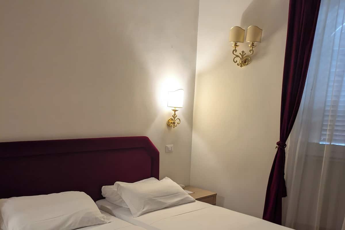 A double bed with white linens, a red headboard, and a wall-mounted light fixture.