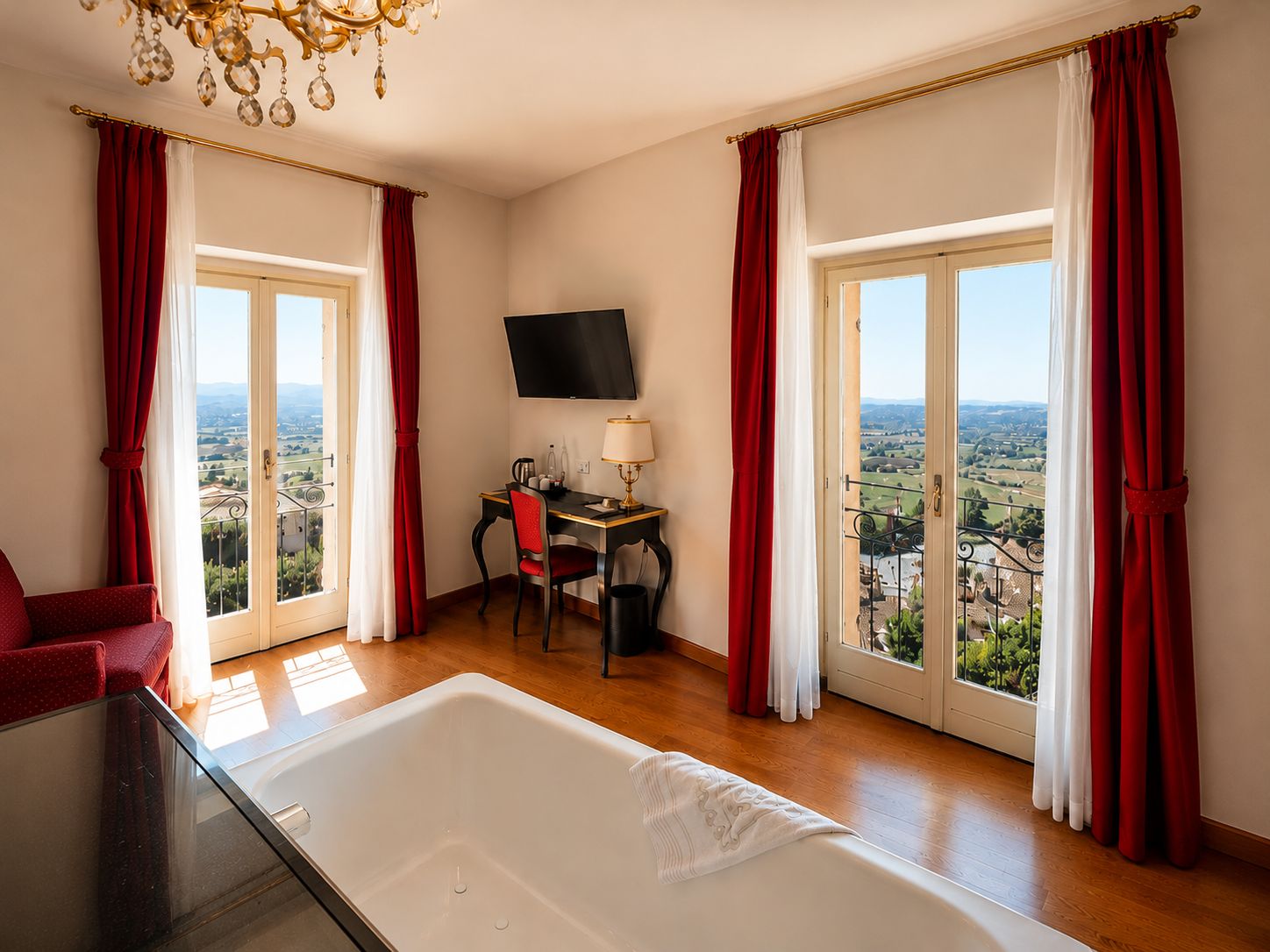 A hotel room with a large window, a desk, a chair, a TV, and a bathtub.
