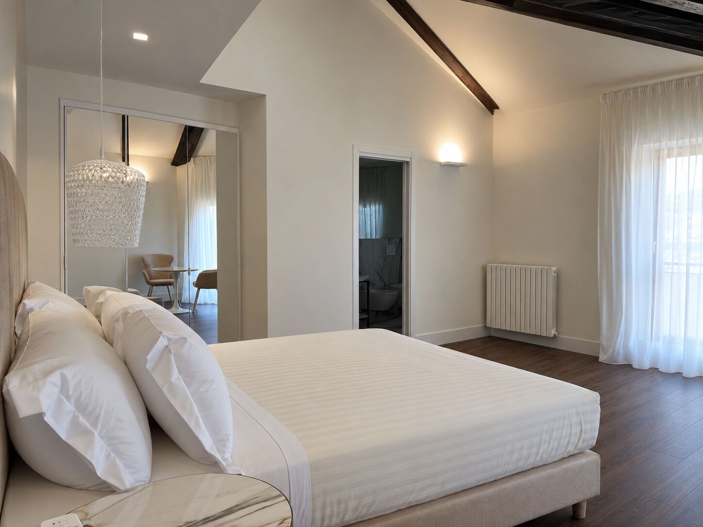 A modern bedroom with a large bed, a bedside table, a hanging light fixture, and a view of a bathroom.