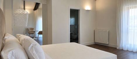 A modern bedroom with a large bed, a bedside table, a hanging light fixture, and a view of a bathroom.