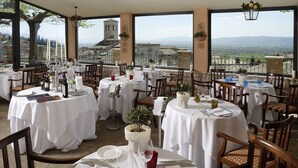 A restaurant with multiple tables set for dining, large windows offering scenic mountain views, and traditional European architecture. - Giotto Hotel & Spa (Assisi)