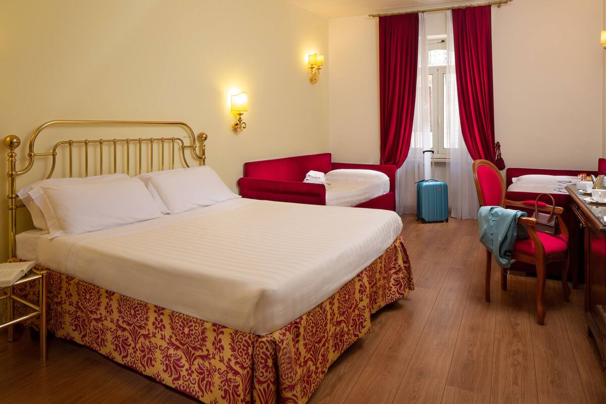 A hotel room with a large bed, a desk, a chair, and a suitcase.