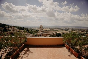 Una terraza con plantas en macetas, vista a un pueblo con una torre y cielo despejado.
