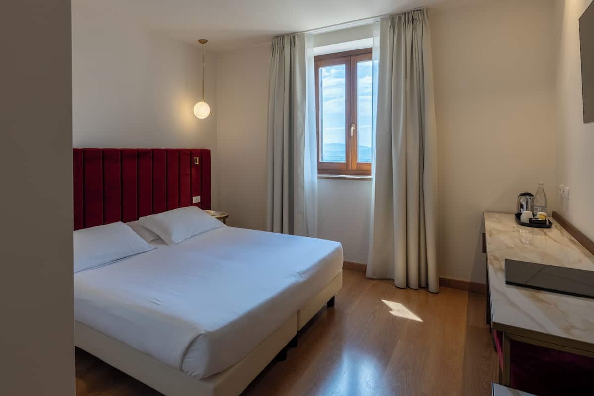 A hotel room with a bed, a nightstand, a desk, and a window with curtains.