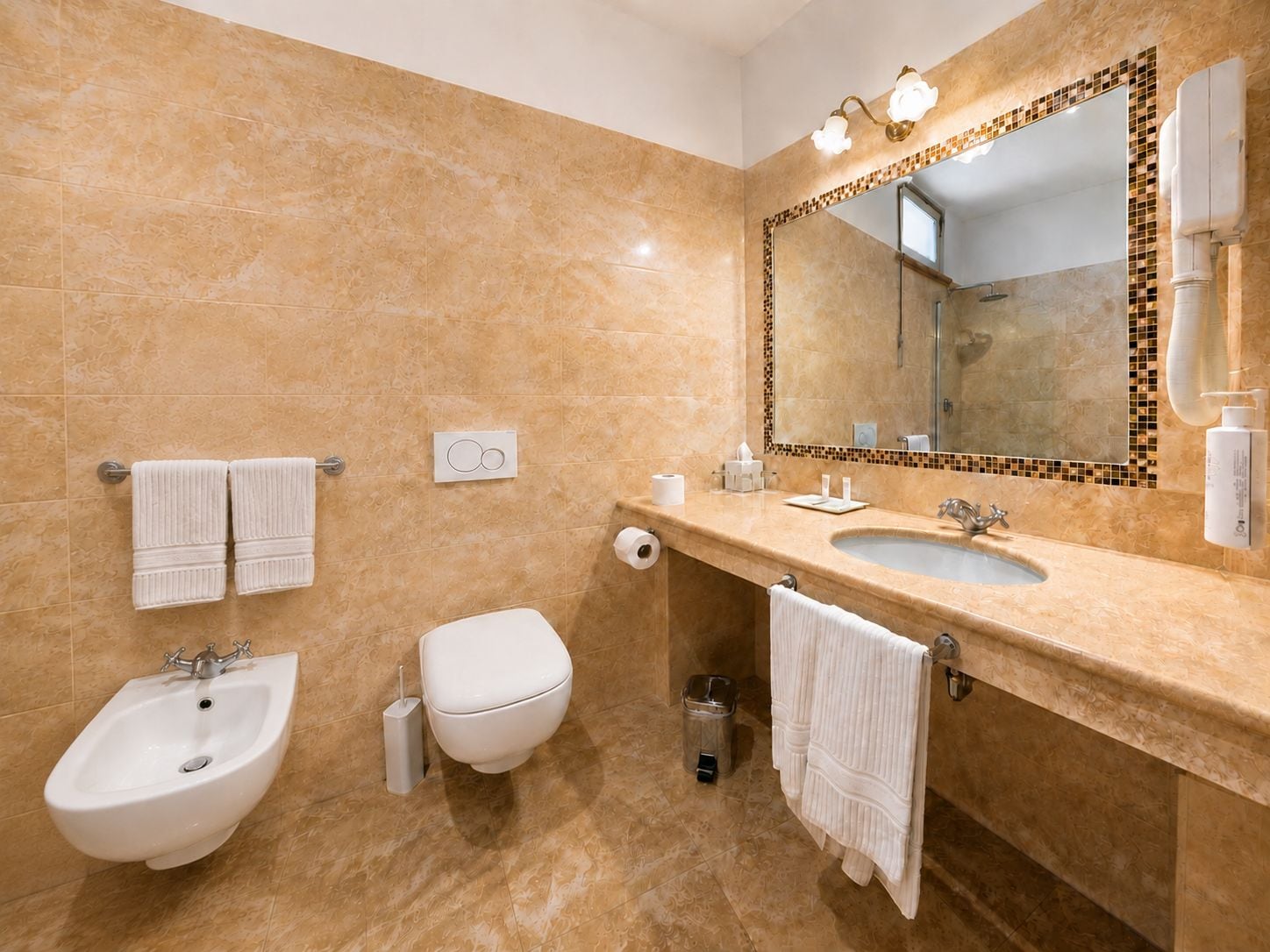 A bathroom with a bidet, toilet, sink, and a large mirror with a mosaic border.