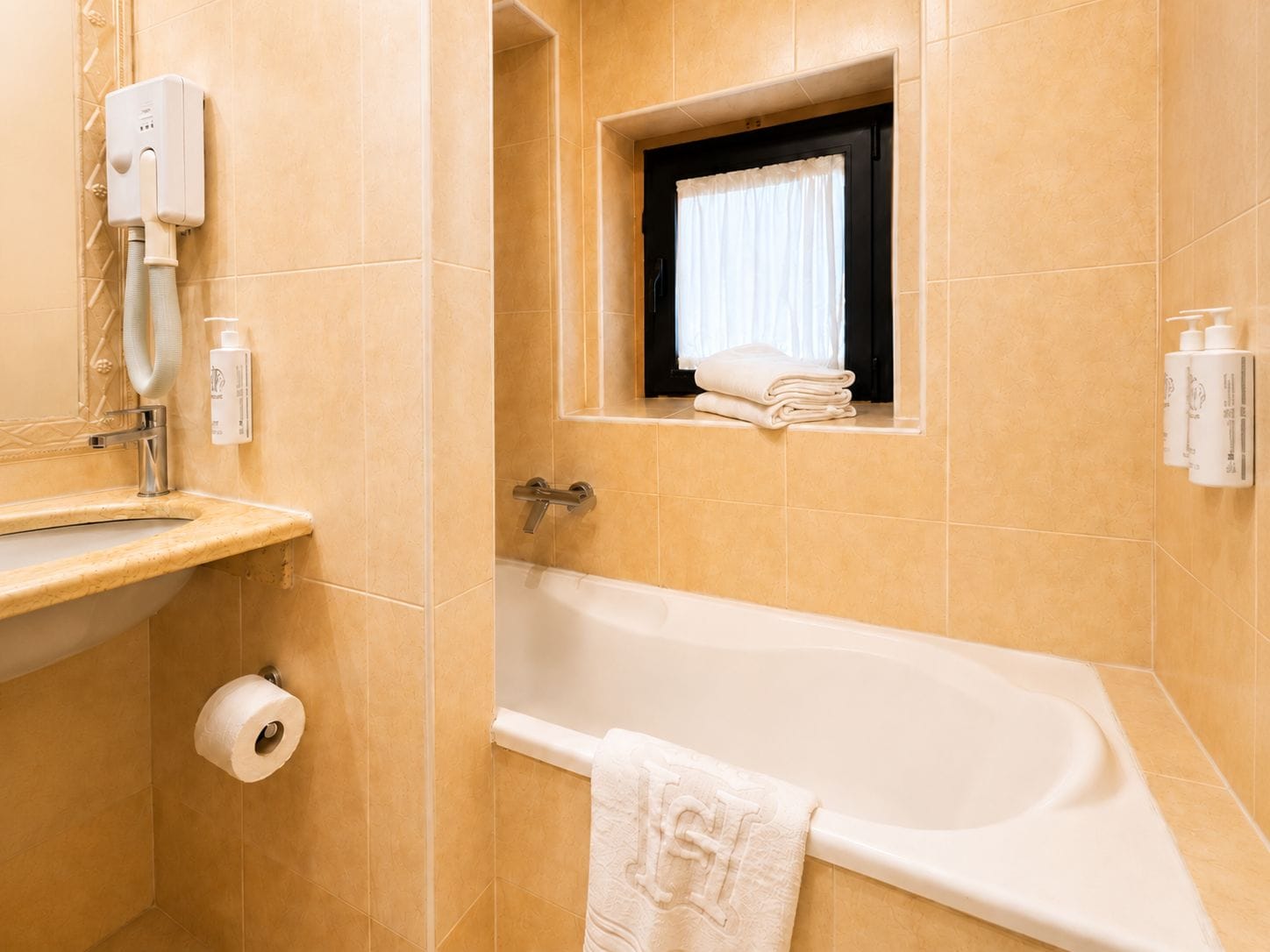 Un baño con bañera, toallero, ventana con cortina y secador de manos.