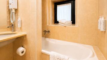 A bathroom with a bathtub, a towel rack, a window with a curtain, and a hand dryer.