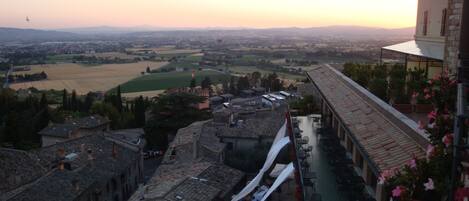 Una terraza con mesas y sillas, con vistas a un valle con campos y colinas lejanas.