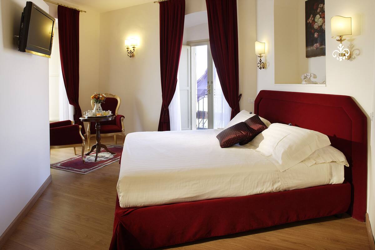 A hotel room with a large bed, a desk with a chair, a TV, and a painting on the wall.