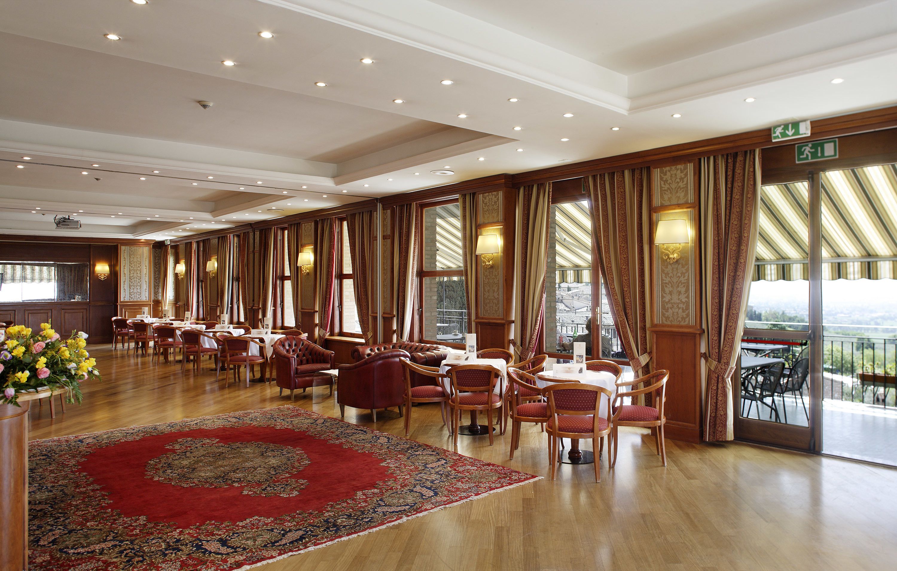 Un comedor espacioso con suelo de madera, cortinas rojas y beige, y una alfombra grande de color rojo.