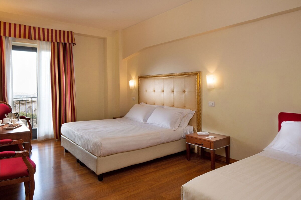 Habitación de hotel con una cama grande, una mesita de noche, una silla y vistas al exterior.