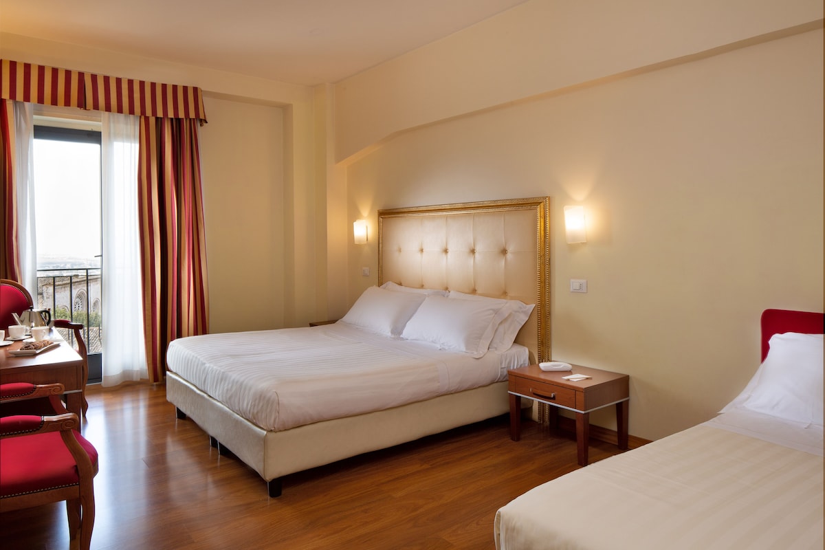 Una habitación de hotel con una cama grande, una mesita de noche, un escritorio con silla y una ventana con cortinas.