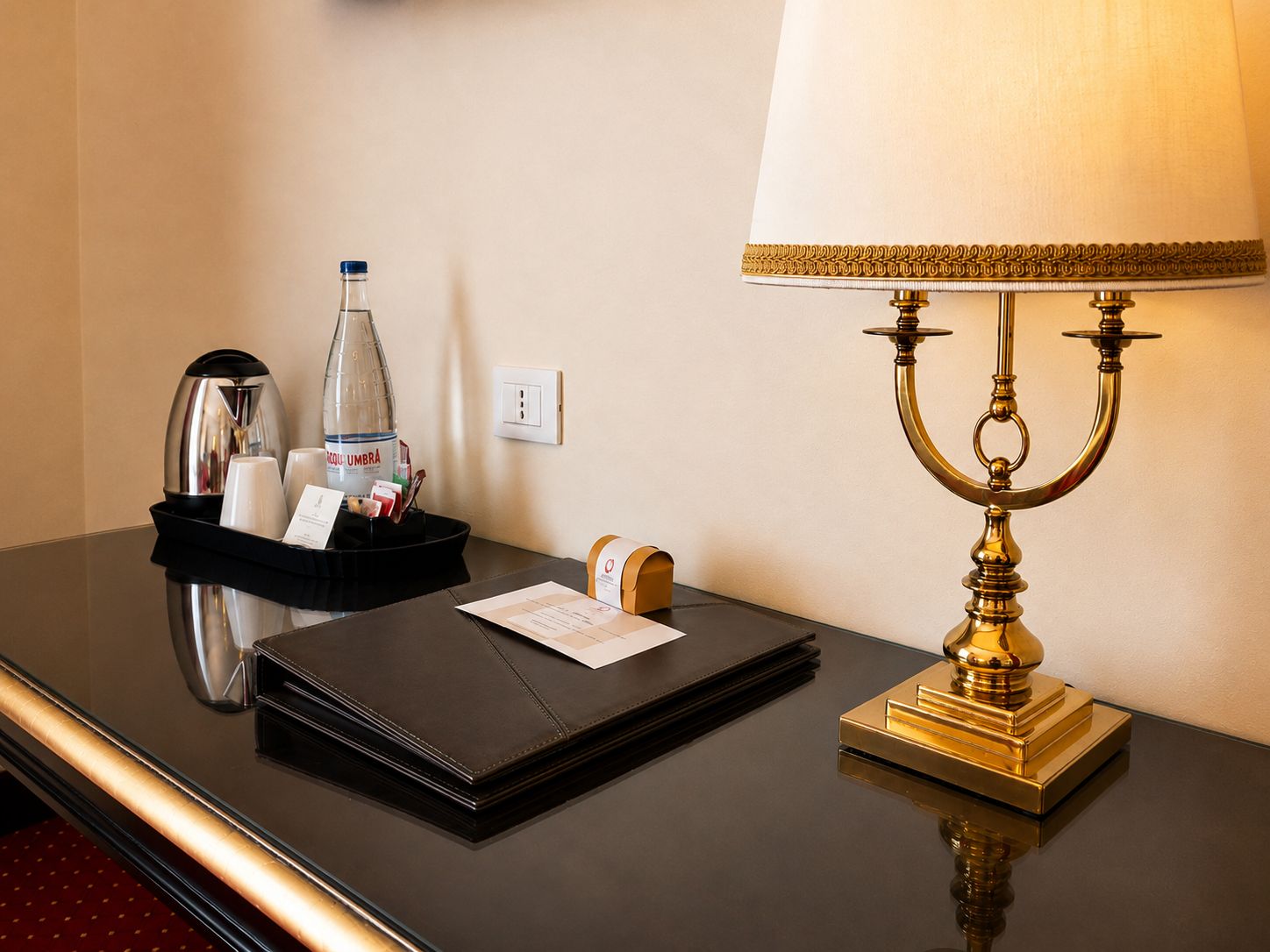 A hotel room desk with a black tray holding a water bottle, a coffee maker, and a notepad.