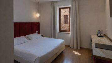 Una habitación de hotel con una cama, una mesita de noche, una ventana con cortinas y una pequeña mesa con lámpara.