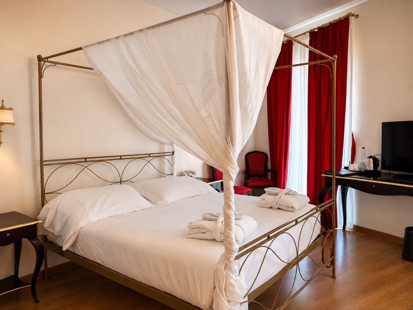 Un lit à baldaquin avec du linge de lit blanc et un ciel de lit, un bureau avec une télévision et une chaise, dans une chambre d’hôtel.