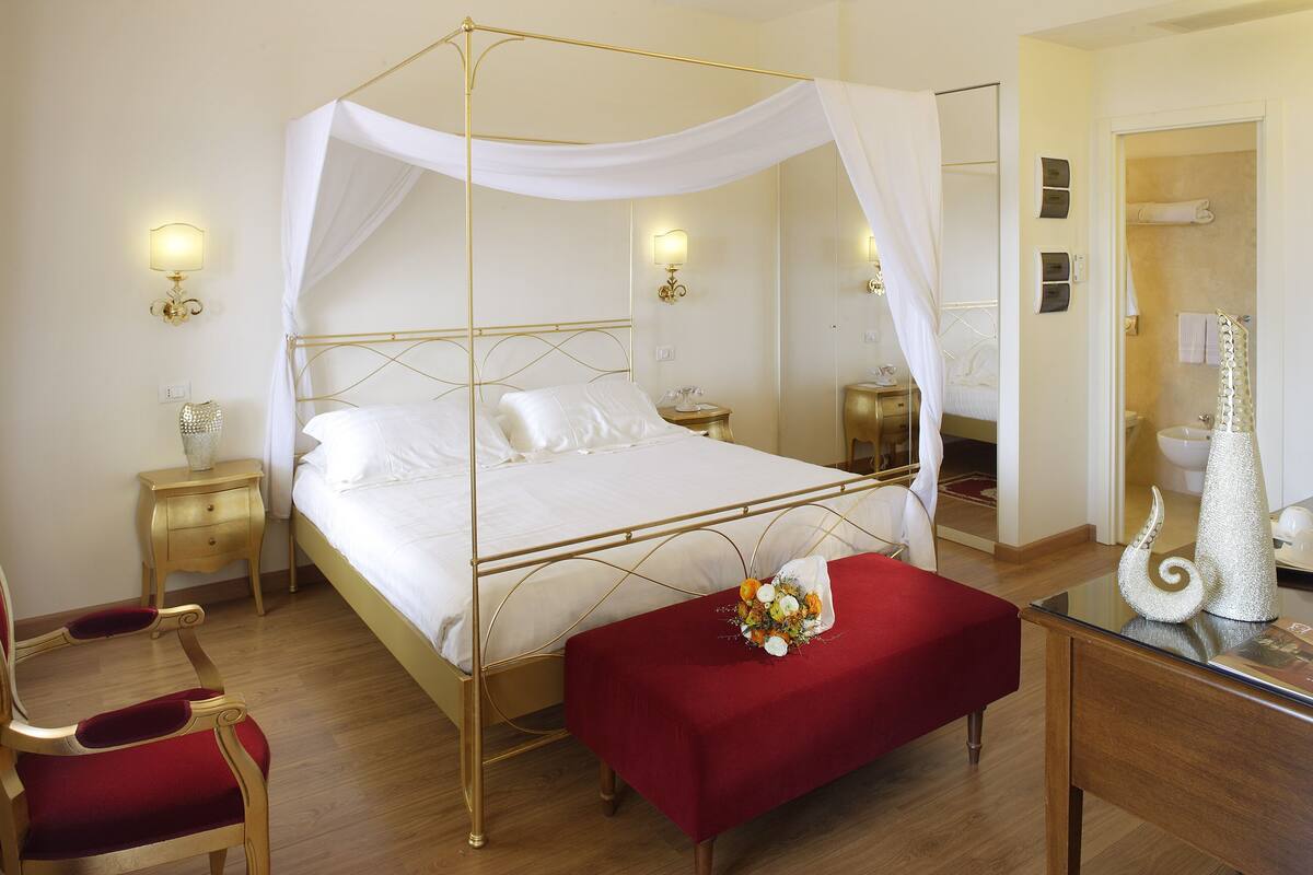 A four-poster bed with a canopy, bedside tables, a red bench, and a mirror.