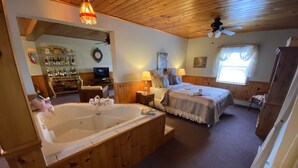 A room with a large wooden bathtub, a bed with a blanket, a television, and a wooden ceiling. - Savannah House Wine Country Inn & Cottages (Himrod)