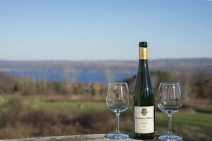 Una botella de vino Riesling 2014 de la viña Hermann J. Wiemer con dos copas vacías sobre una superficie de madera, frente a un paisaje pintoresco.