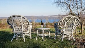 Two wicker chairs and a small table with a bottle and glass, set on a grassy area with a view of a lake and hills in the background. - Savannah House Wine Country Inn & Cottages (Himrod)