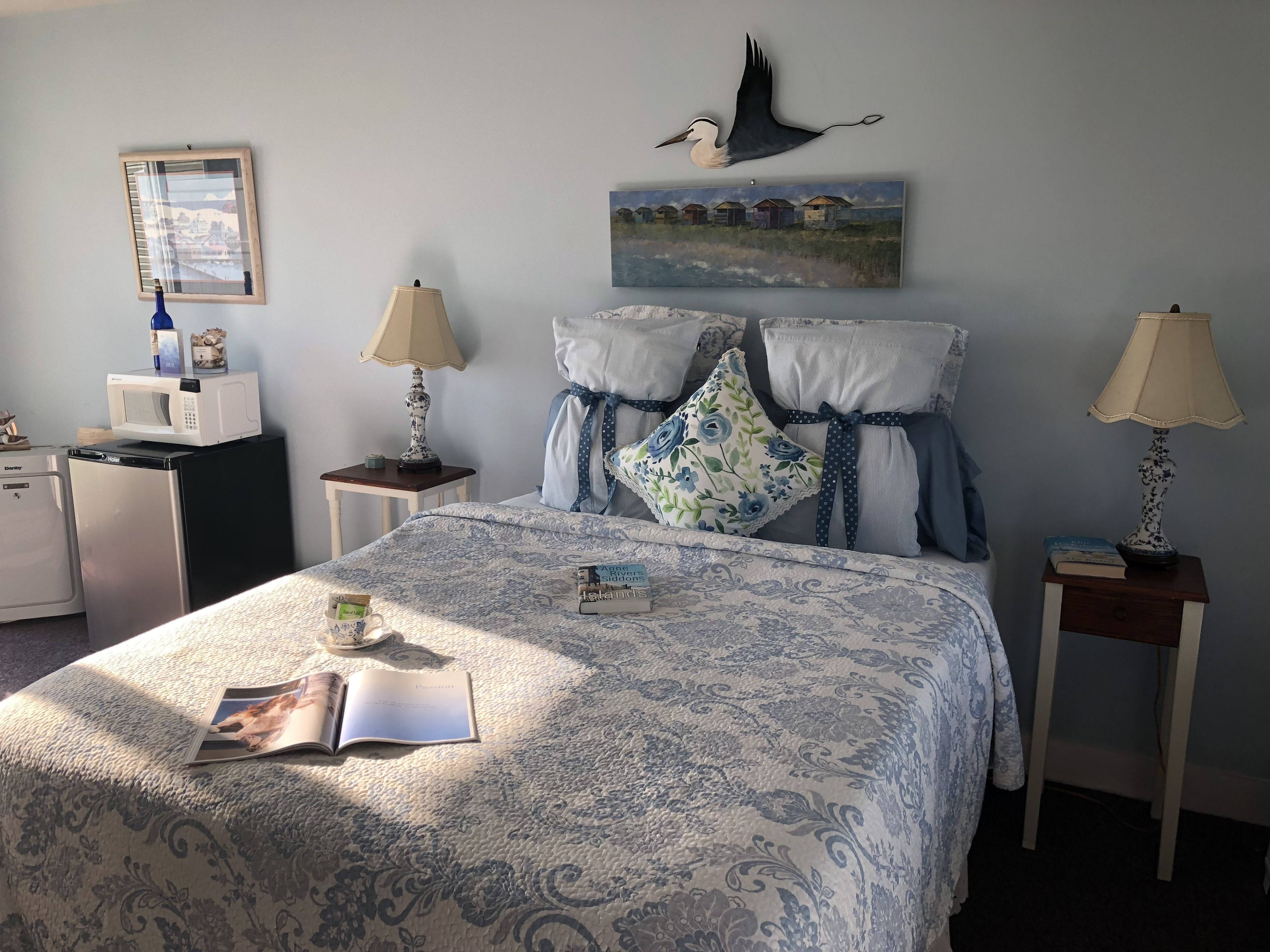 A neatly arranged bedroom with a bed, bedside tables, lamps, a microwave, and a refrigerator.