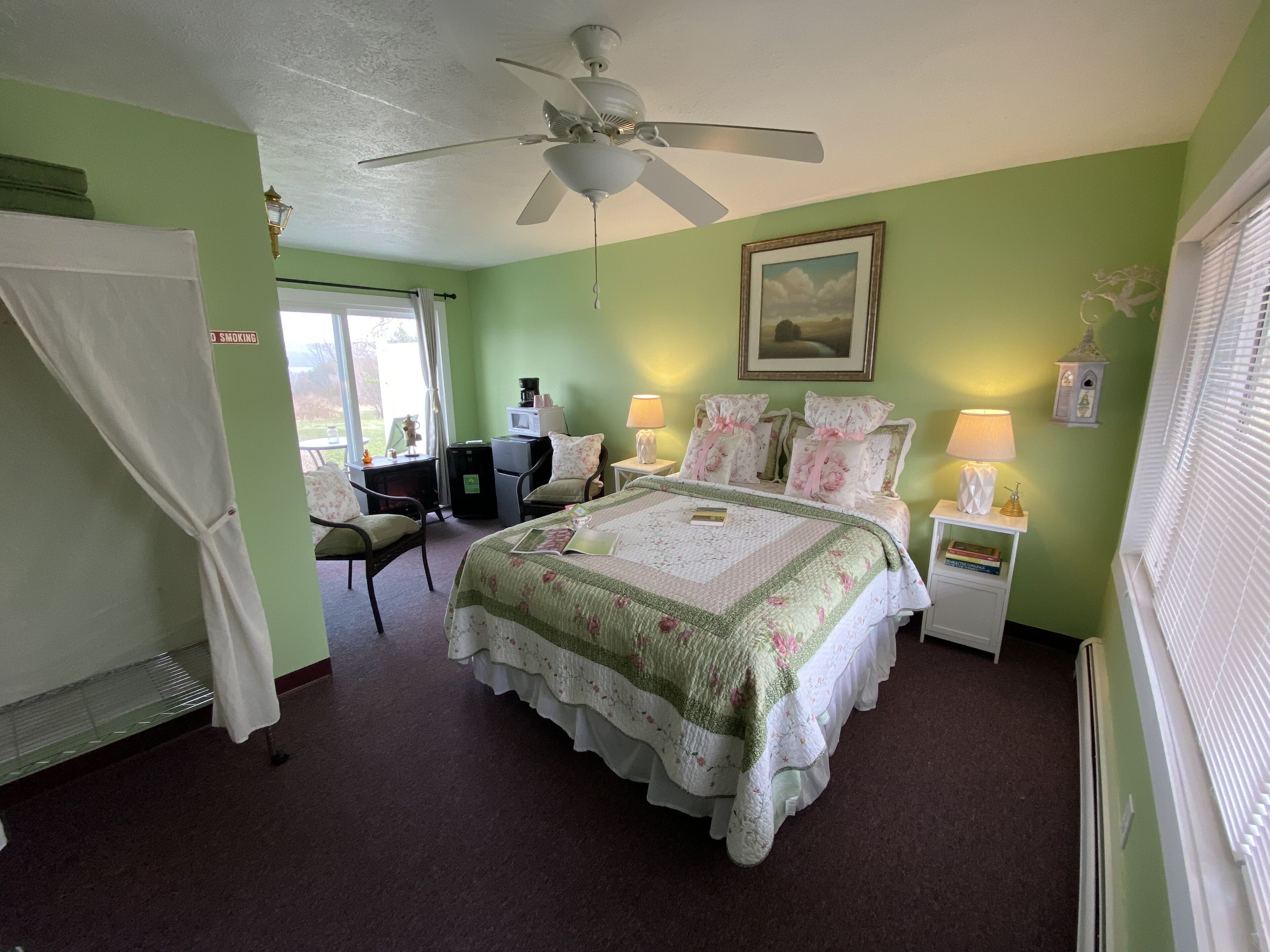 A bedroom with a bed, a desk, a chair, a ceiling fan, and a window with blinds.