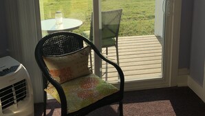 A room with a sliding glass door leading to an outdoor patio. Inside, there is a chair with a cushion and a table with a glass. - Savannah House Wine Country Inn & Cottages (Himrod)