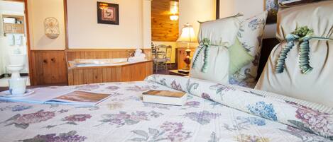 A bedroom with a floral bedspread, a wooden headboard, a bedside table with a lamp, and a view of the bathroom.