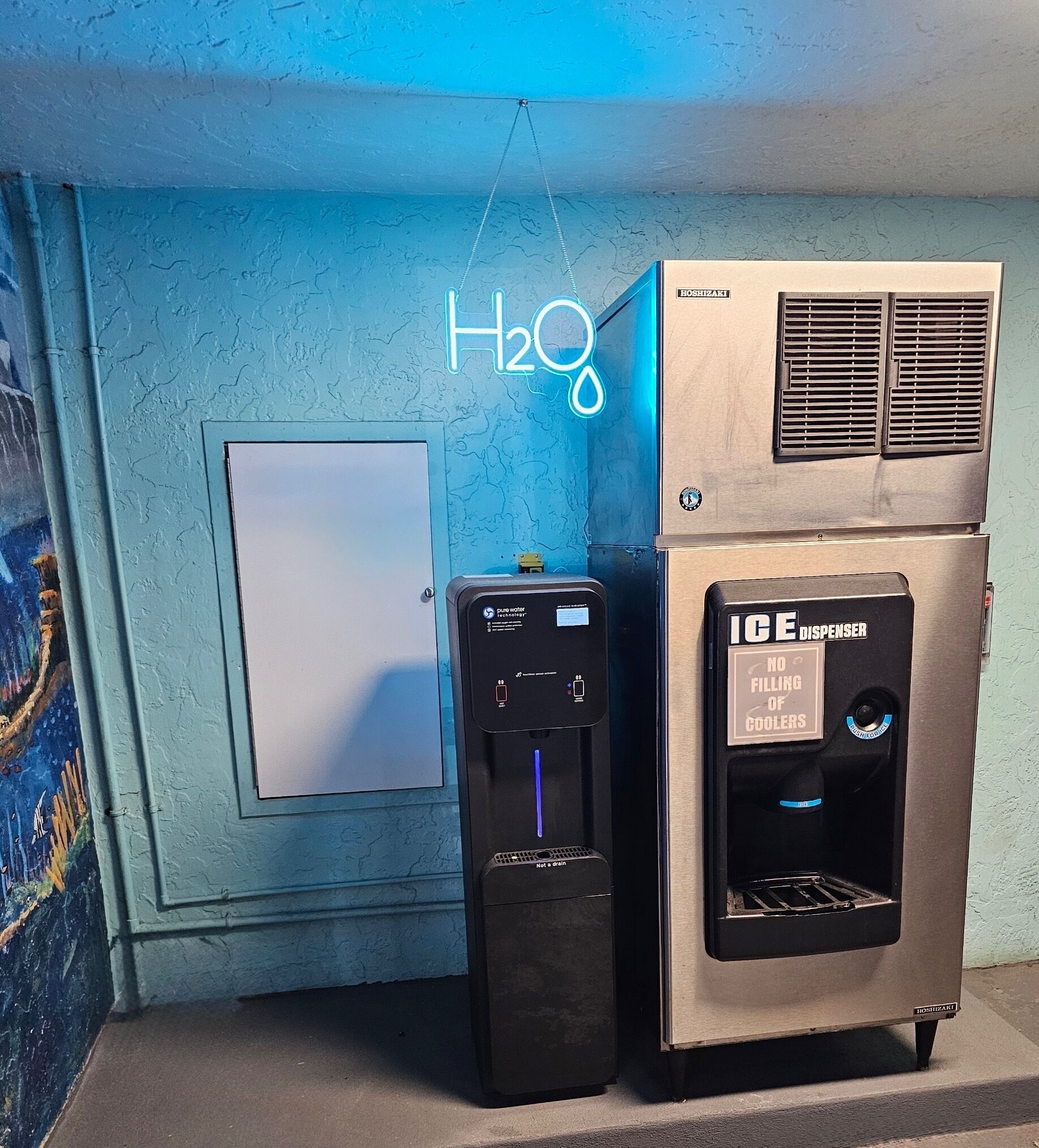 Un dispensador de agua y un dispensador de hielo uno al lado del otro, con una pared azul y una puerta al fondo.