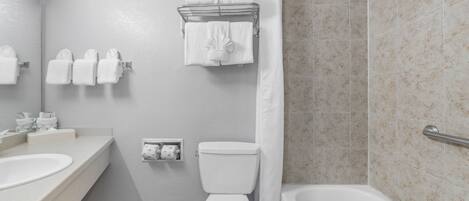 Une salle de bain avec une baignoire, des toilettes et un lavabo. Plusieurs serviettes sont suspendues sur un porte-serviettes.