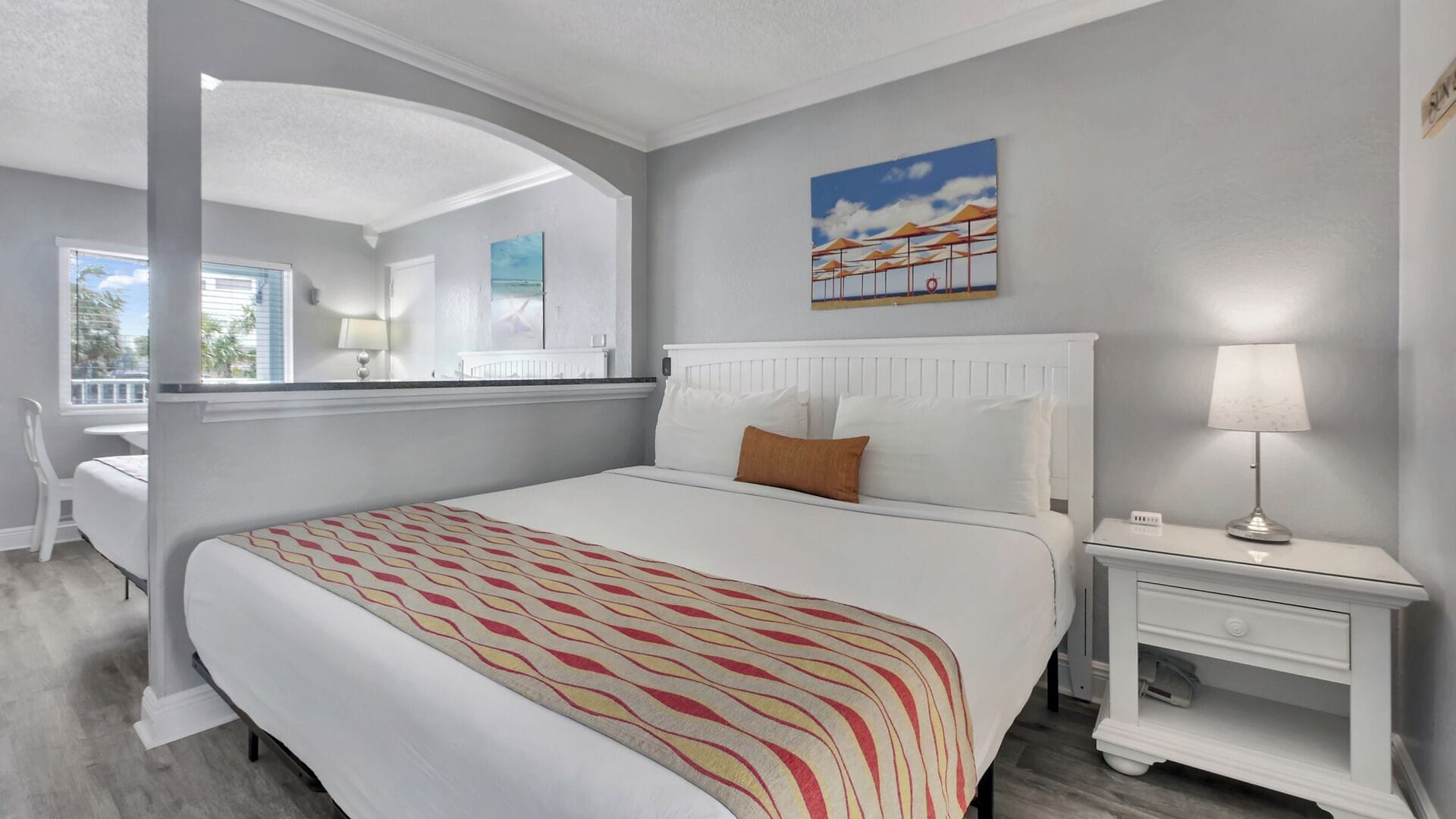 A bedroom with a bed, a nightstand, a lamp, a painting, and a window with a view.