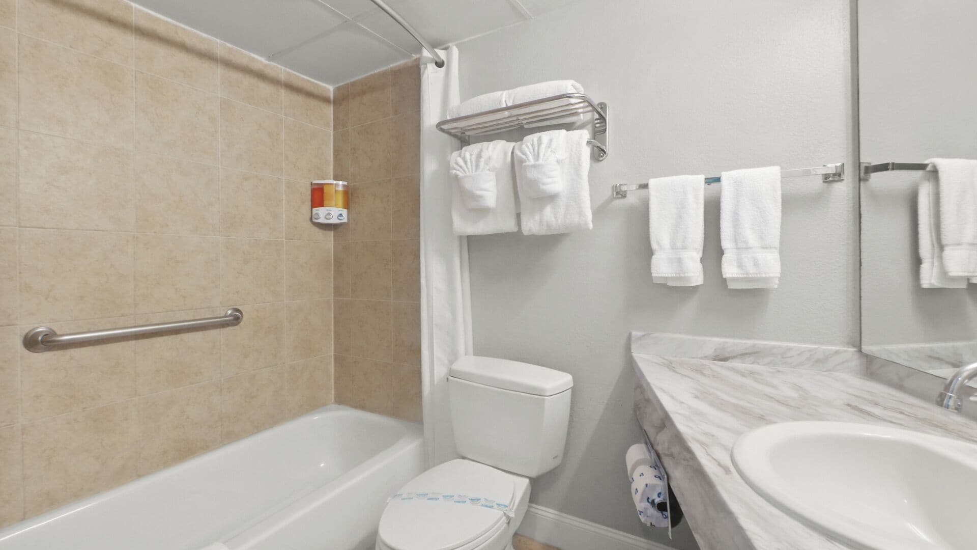 A bathroom with a bathtub, toilet, and sink. There is a towel rack with multiple towels and a shower curtain.