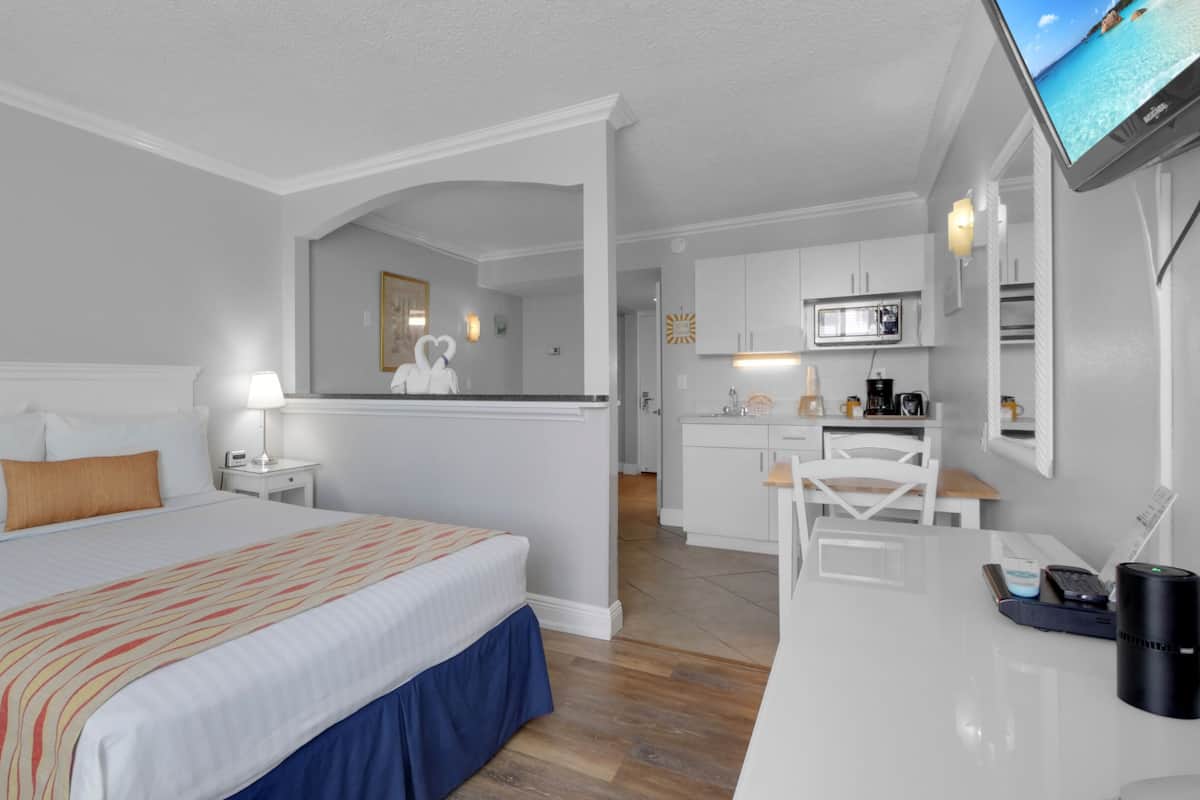 A hotel room with a bed, a desk, a chair, a TV, and a kitchen area.