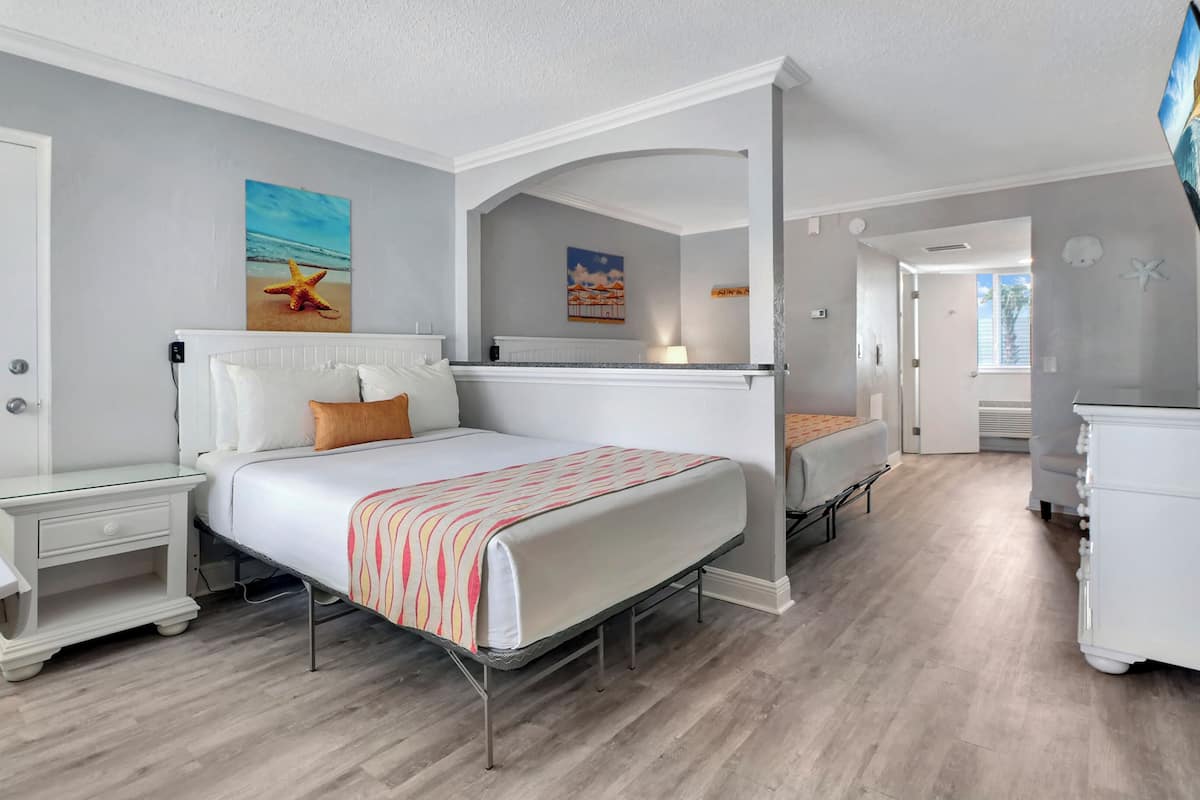 A bedroom with a bed, a nightstand, a dresser, and a painting of a beach scene.