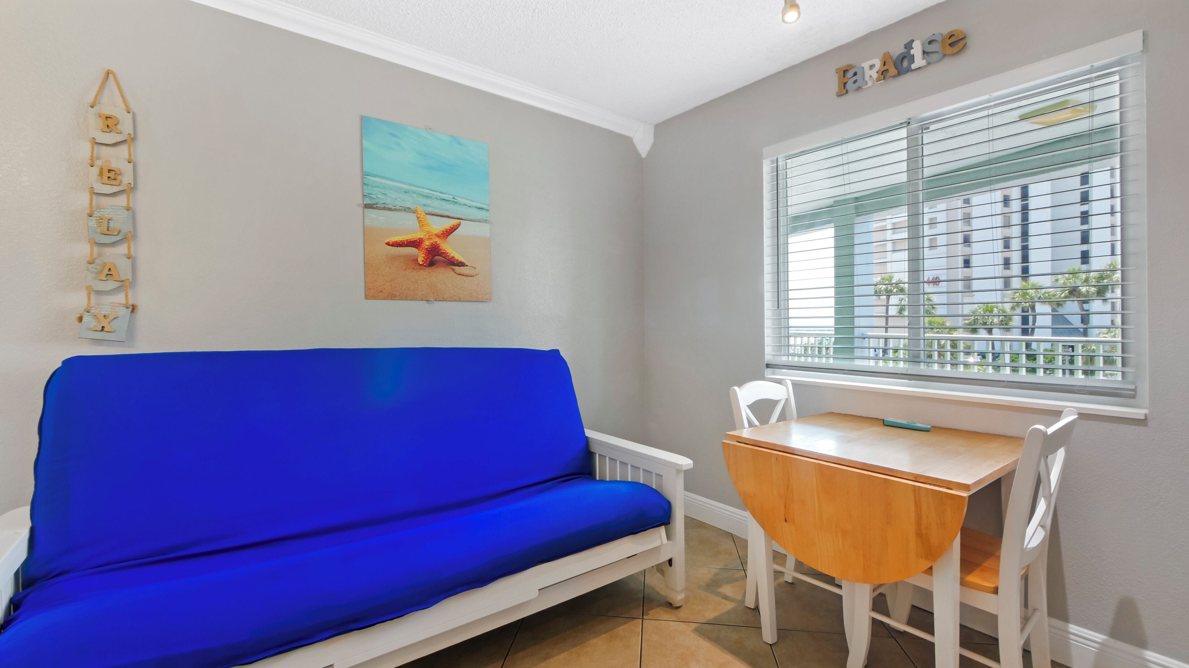 Una habitación con un sofá azul, una mesa de madera y una ventana con persianas.