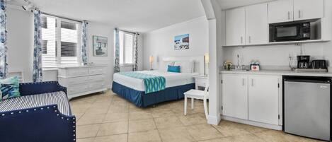 Una habitación de hotel compacta con cama, escritorio, silla, kitchenette y baño.