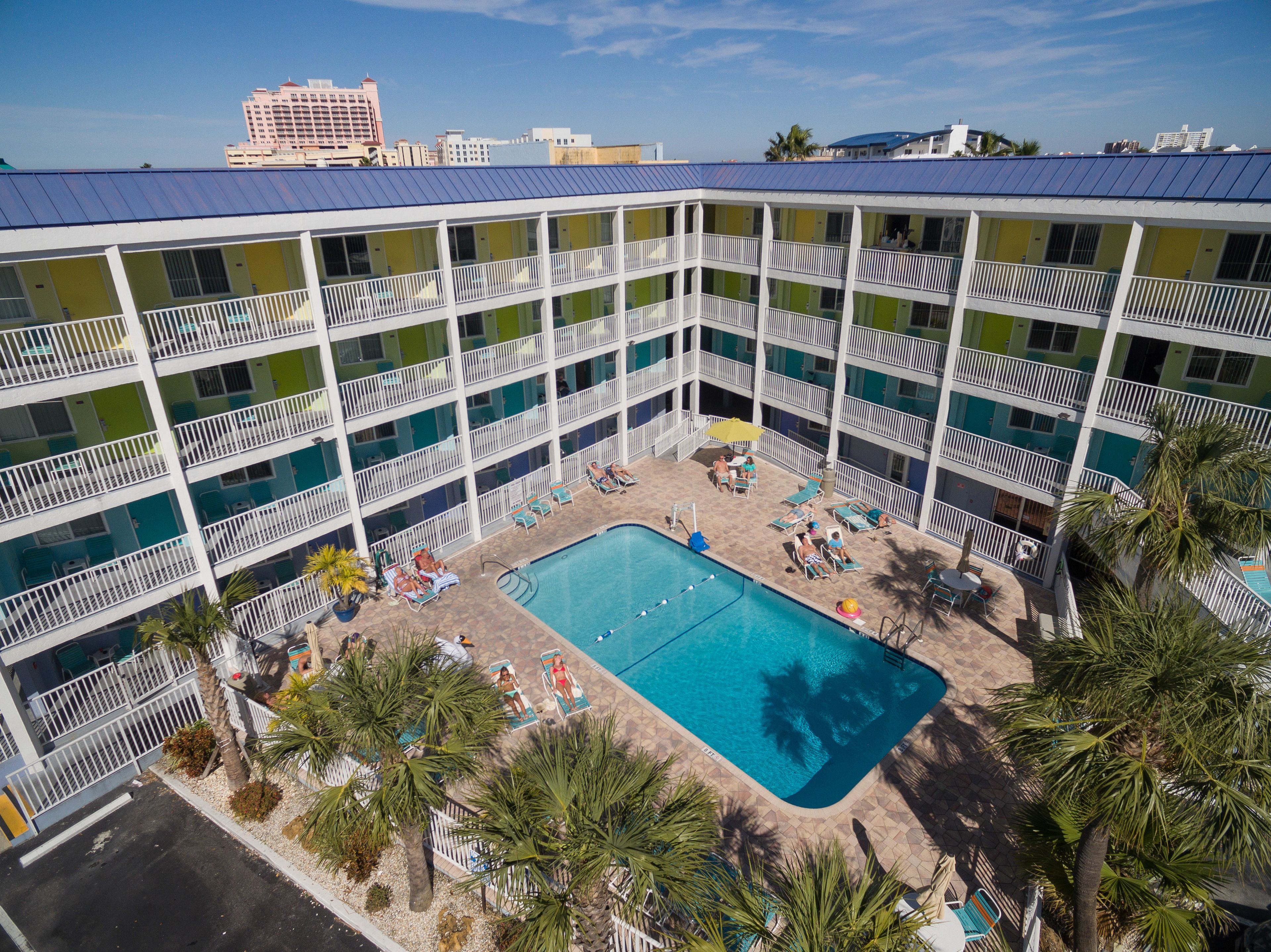 Un hôtel à plusieurs étages doté d’une piscine sur le toit, entourée de palmiers et de chaises longues.