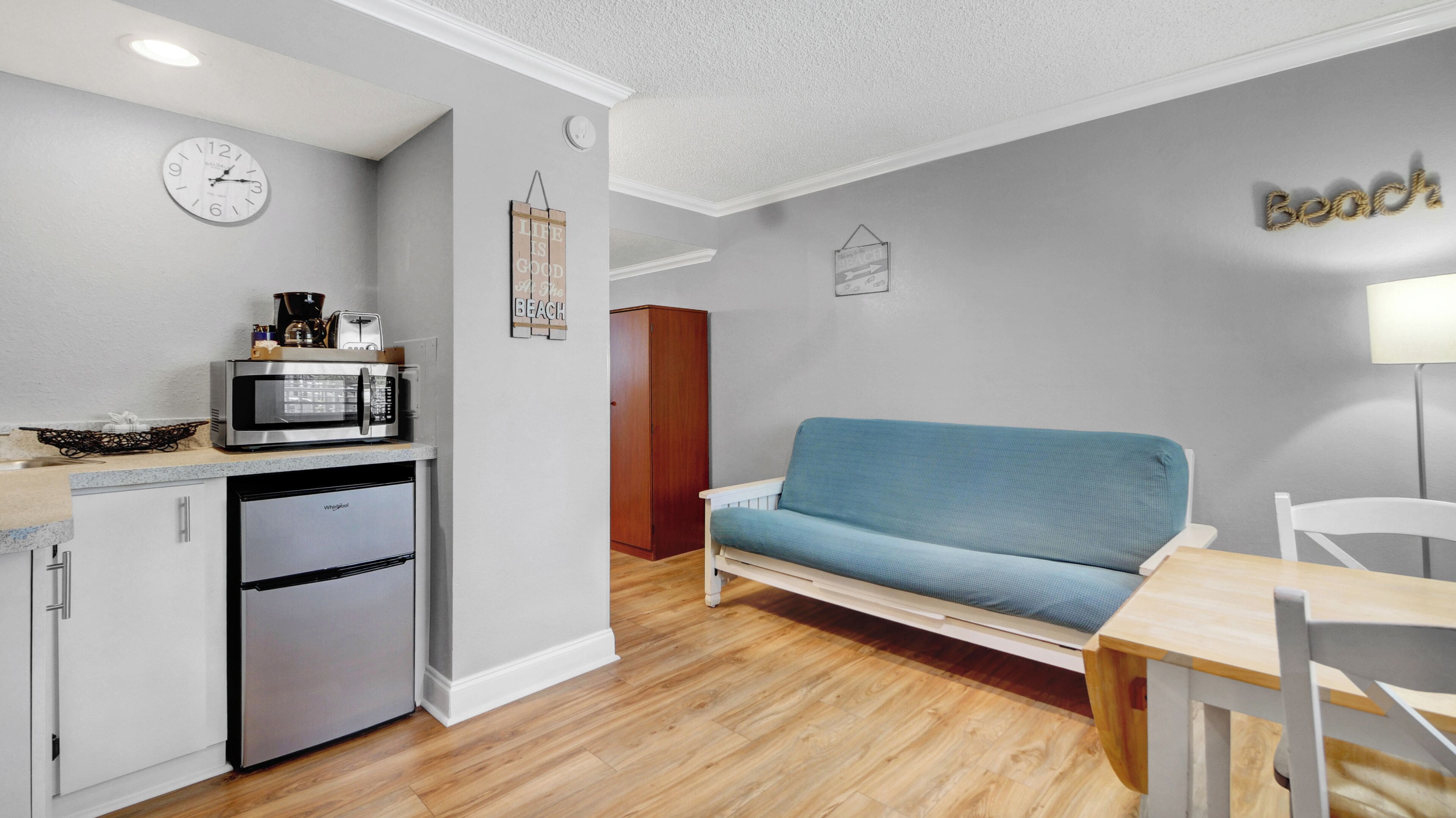 A compact living space with a kitchenette, a sofa, a dining table, and a clock on the wall.