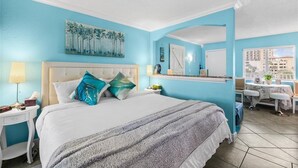 A hotel room with a bed, bedside table, lamp, and a view of the city.