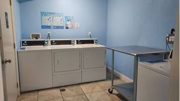 A laundry room with a washing machine, dryer, and a metal cart.