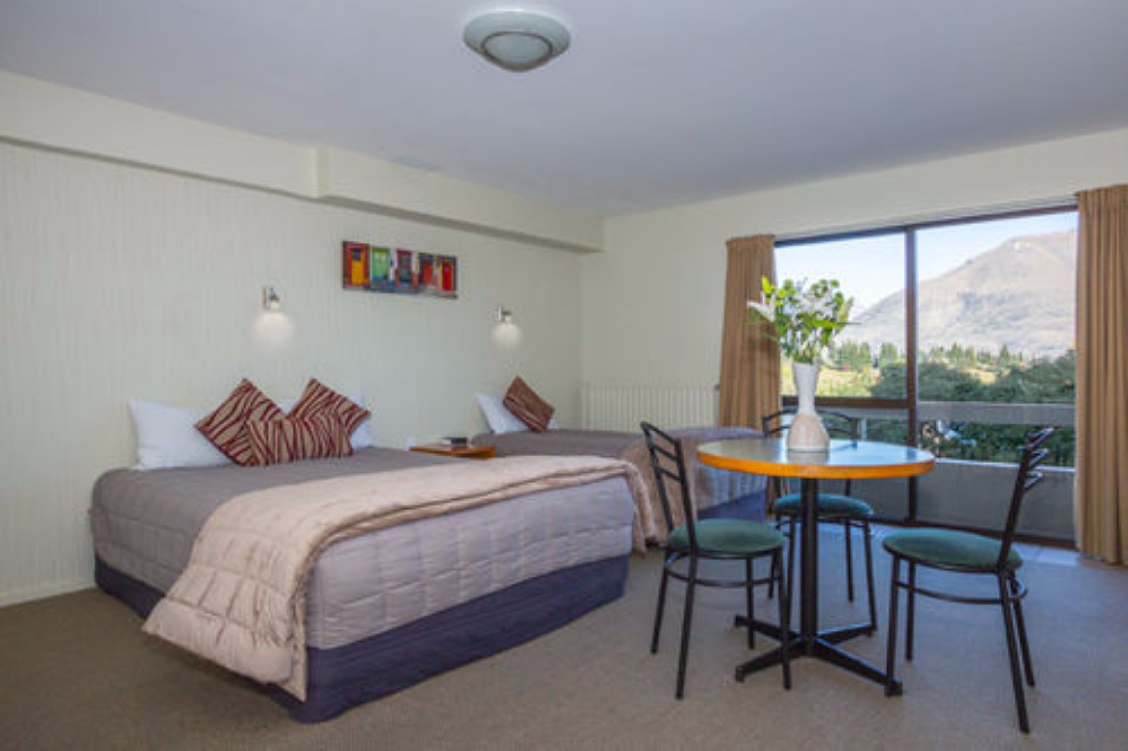 Een hotelkamer met een bed, een kleintje tafeltje met stoelen, een raam met gordijnen en uitzicht op de omgeving.